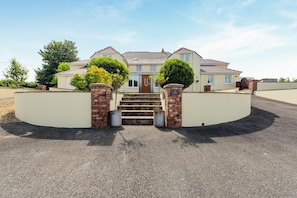 A two-story house with a front entrance, a driveway, and a landscaped area with trees. - 6 Bed in Moreton (oc-h45423) (Moreton)