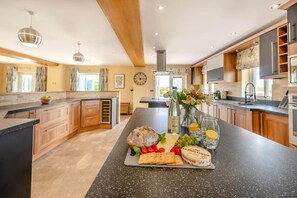 A modern kitchen with a central island, wooden cabinets, and a large window. - 6 Bed in Moreton (oc-h45423) (Moreton)