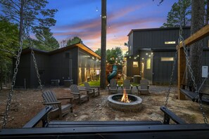 A backyard with a fire pit, Adirondack chairs, a swing set, and a slide. - The Cedarwood Collective · Indoor Pool, Theatre, Putt-Putt & Gameroom | Sleeps 27! (Broken Bow)