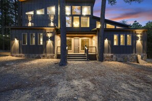 Ein zweistöckiges Haus mit steinernen Fundament, zahlreichen Fenstern und einer Veranda mit Stufen.