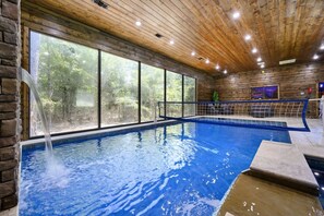 Ein Innenpool mit Wasserfall, umgeben von großen Fenstern und Holzwänden.