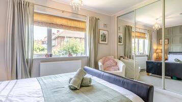 A bedroom with a bed, a chair, a large mirror, and a window with curtains.