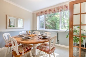 A dining area with a round table set for four, white chairs with patterned cushions, a window with a view of greenery, and a door with a glass panel. - 4 Bed in Chesterfield (oc-w45546) (Chesterfield)