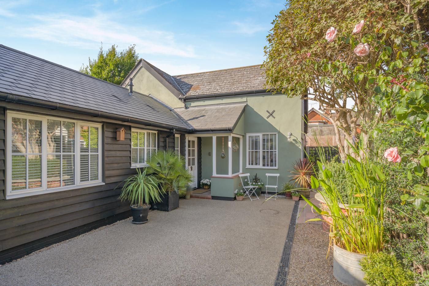A house with a gravel driveway, a small patio with chairs, and a garden with various plants and flowers.