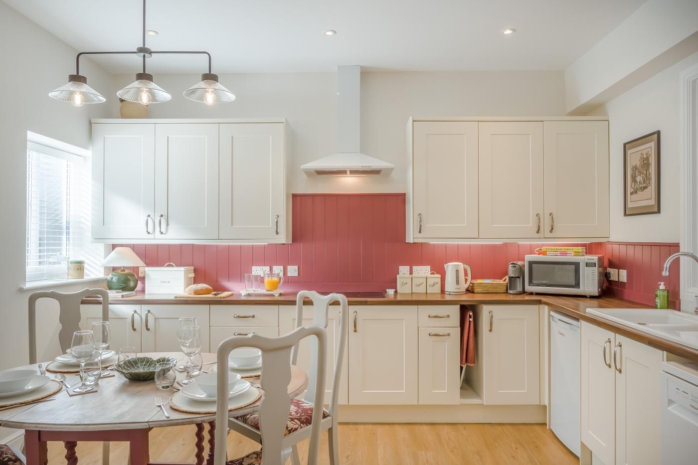 A kitchen with white cabinets, a pink backsplash, and a dining area with a table set for four.