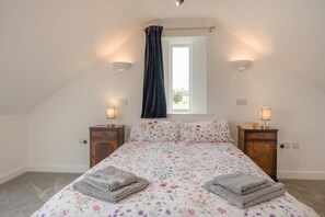 Ein Schlafzimmer mit einem Bett, zwei Nachttischen, einem Fenster mit Vorhängen und Wandleuchten.