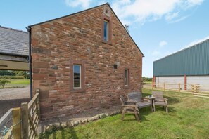 Ein Steinhaus mit zwei Fenstern und einer kleinen Außenbestuhlung mit Tisch und Stühlen.