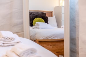 Ein ordentlich bezogenes Bett mit weißen Leinen und einem grünen Kopfkissen in einem Hotelzimmer.