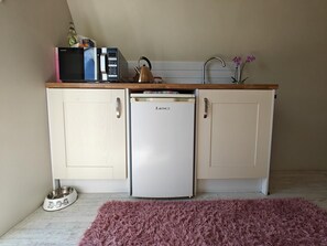 Eine kleine Küchenzeile mit Mikrowelle, Wasserkocher und kleinem Kühlschrank.