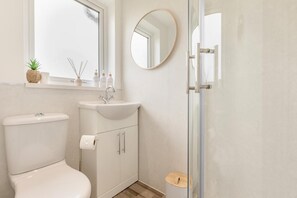 A bathroom with a toilet, sink, mirror, and a small window with a plant. - 3 Bed in Leek (oc-l45949) (Leek)