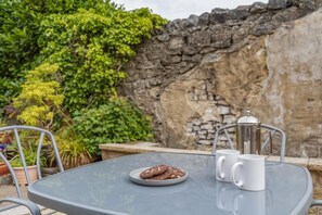 A table with a plate of cookies, a coffee pot, and a mug, set against a stone wall and greenery. - 2 Bed in Buxton (oc-p45950) (Buxton)