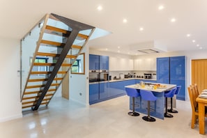 A modern kitchen with blue cabinets, a dining area with blue chairs, and a spiral staircase.