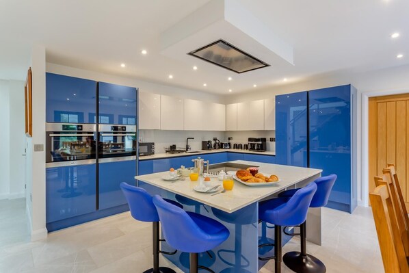 Una cocina moderna con una isla central, taburetes de bar y una mesa de comedor lista para el desayuno.