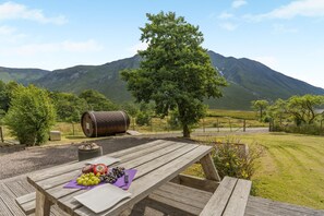 A wooden picnic table with a view of mountains, a barrel, and a tree. - 4 Bed in Glen Etive (oc-h45919) (Glenetive)