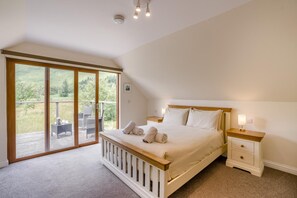 Ein Schlafzimmer mit einem großen Bett, einem Nachttisch, einer Nachttischlampe und einer Schiebetür zu einem Außenbereich mit Tisch und Stühlen.