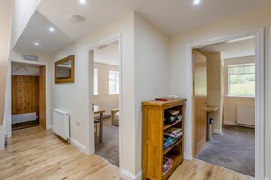 A hallway with wooden flooring, a radiator, a wooden cabinet with books, and a door leading to another room. - 4 Bed in Glen Etive (oc-h45919) (Glenetive)