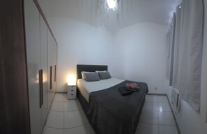 Ein Schlafzimmer mit einem Bett, Nachttischen, einem Kleiderschrank und einem Fenster mit Vorhängen.