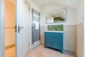 Ein Badezimmer mit einer weißen Tür, einem Handtuchhalter, einem blauen Schrank und einem Spiegel mit einer grün gefliesten Rückwand.