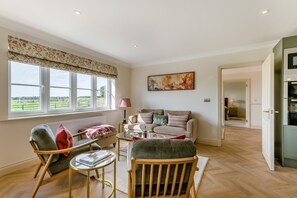 Ein geräumiges Wohnzimmer mit einer Couch, Sesseln, einem Couchtisch und Blick ins Freie durch große Fenster.