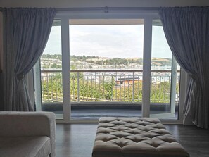 A room with a large sliding glass door leading to a balcony with a view of a marina and hills. - 1 Bed in Kingswear (oc-b45934) (Dartmouth)