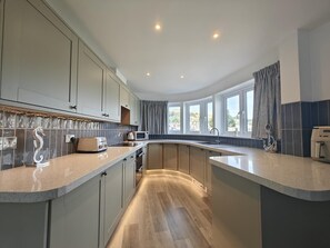 A modern kitchen with a curved island, built-in appliances, and large windows offering a view. - 1 Bed in Kingswear (oc-b45934) (Dartmouth)