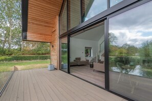A modern house with a deck, large sliding glass doors, and a view of a garden. - 3 Bed in Doddington (oc-l45736) (Doddington)