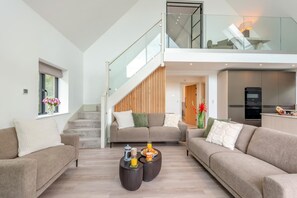 A modern living room with a staircase leading to a loft, a kitchen with built-in appliances, and a dining area. - 3 Bed in Doddington (oc-l45736) (Doddington)