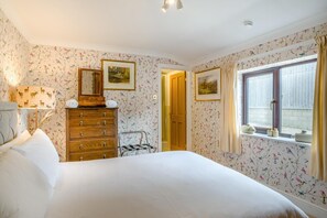 A bedroom with floral wallpaper, a wooden dresser, a bed, a window with curtains, and a door leading to another room. - 8 Bed in Gillingham (oc-w45983) (Gillingham)
