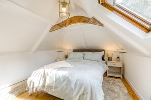 Ein Schlafzimmer mit schrägem Dach, einem Bett mit floralem Überwurf, Nachttischlampen und einem Fenster mit Aussicht.