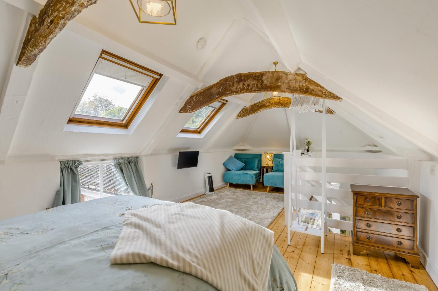 A bedroom with a sloped ceiling, a bed, a TV, a dresser, and two chairs.