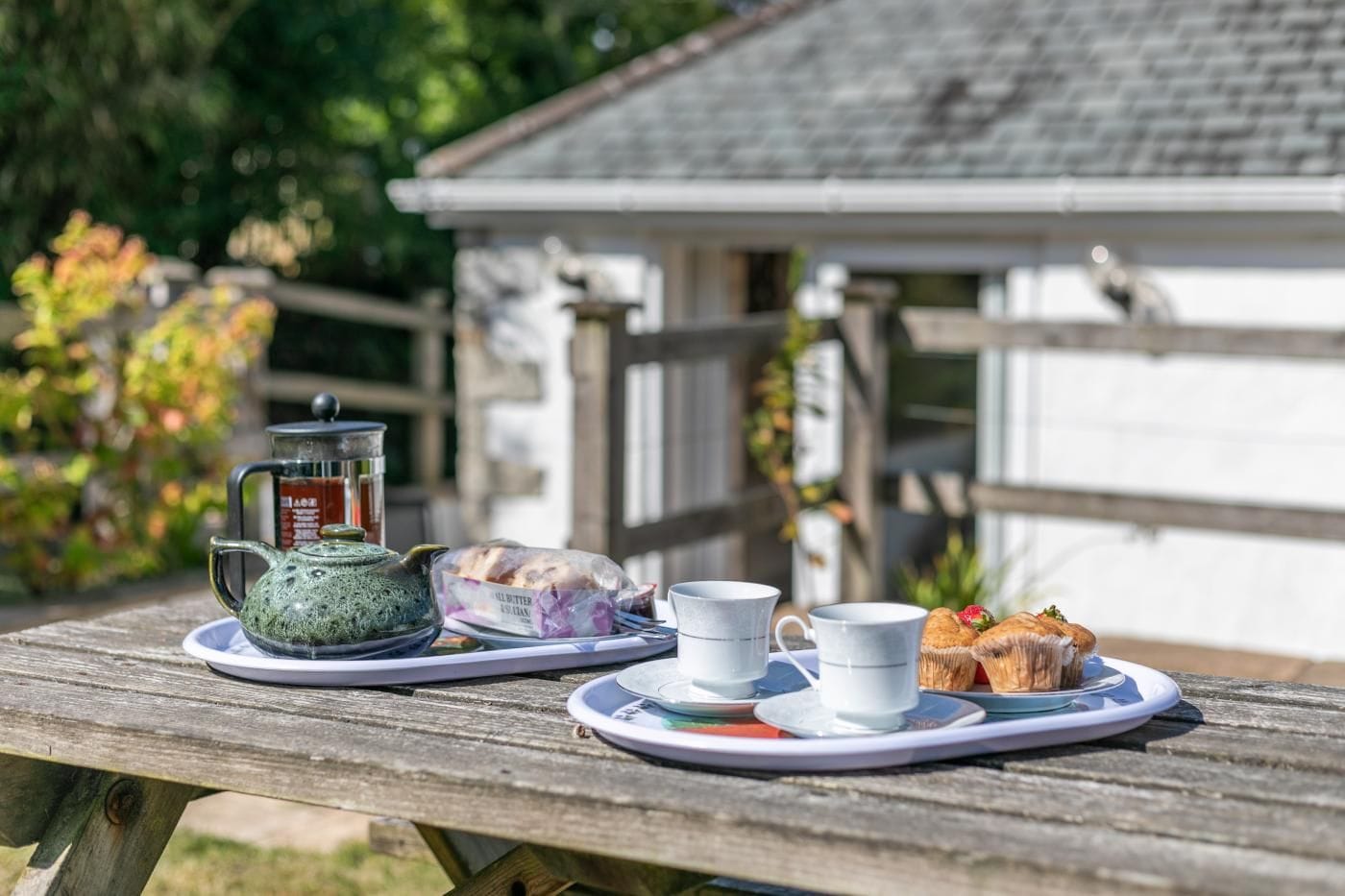 A picnic setup on a wooden table with a teapot, cups, and pastries.