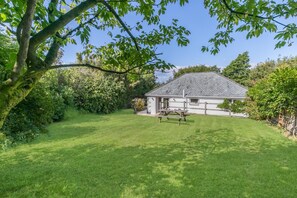 Ein Haus mit geneigtem Dach, einem umzäunten Garten und einem Picknicktisch.