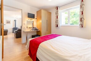 Ein Schlafzimmer mit einem Bett, einem Schreibtisch inklusive Spiegel, einem Fernseher und einem Fenster mit Vorhängen.