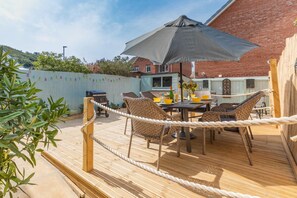 An outdoor patio with a table and chairs, a rope barrier, and a brick building in the background. - 3 Bed in Westward Ho (oc-h45910) (Northam)