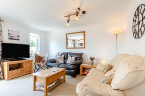 A living room with a television, leather sofa, wooden coffee table, and a large mirror. - 3 Bed in Westward Ho (oc-h45910) (Northam)