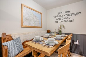Ein Essbereich mit einem Holztisch, gedeckt für sechs Personen, einer Karte an der Wand und einem Wandtext mit der Aufschrift 'Es ist Zeit, Champagner zu trinken und auf den Tischen zu tanzen!'