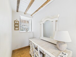 A room with a white dresser, a mirror, a window with a view of a stone wall, and a wooden ceiling. - 2 Bed in Robin Hoods Bay (oc-o45886) (Robin Hood's Bay)