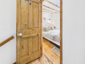 A wooden door leading to a bedroom with a bed, a headboard, and a nightstand. - 2 Bed in Robin Hoods Bay (oc-o45886) (Robin Hood's Bay)