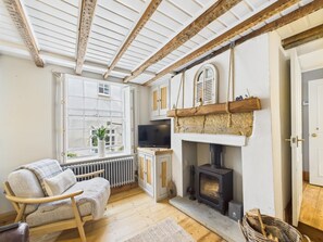 A cozy room with a fireplace, a television, and a window with a view of greenery. - 2 Bed in Robin Hoods Bay (oc-o45886) (Robin Hood's Bay)