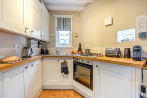 A kitchen with white cabinets, a wooden countertop, a gas stove, a toaster, and a kettle. - 1 Bed in Robin Hoods Bay (oc-o45887) (Robin Hood's Bay)