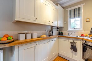 A kitchen with white cabinets, a wooden countertop, a stove, and a window with curtains. - 1 Bed in Robin Hoods Bay (oc-o45887) (Robin Hood's Bay)