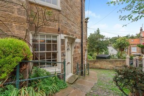 A stone building with a traditional design, a small front garden, and a cobblestone pathway leading to the entrance. - 1 Bed in Robin Hoods Bay (oc-o45887) (Robin Hood's Bay)