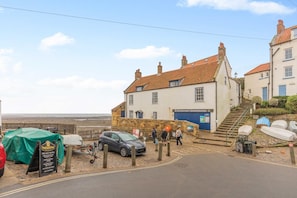 A coastal building with a staircase leading to a second floor, a sign for a visitor center, and a parked car. - 1 Bed in Robin Hoods Bay (oc-o45887) (Robin Hood's Bay)