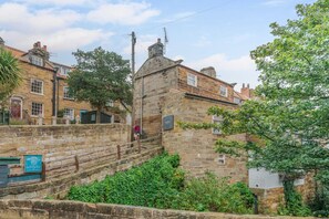 A stone building with a staircase leading up to a door, surrounded by greenery and other buildings. - 1 Bed in Robin Hoods Bay (oc-o45887) (Robin Hood's Bay)