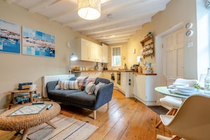 A cozy living room with a sofa, a coffee table, and a dining area with a table set for two. - 1 Bed in Robin Hoods Bay (oc-o45887) (Robin Hood's Bay)