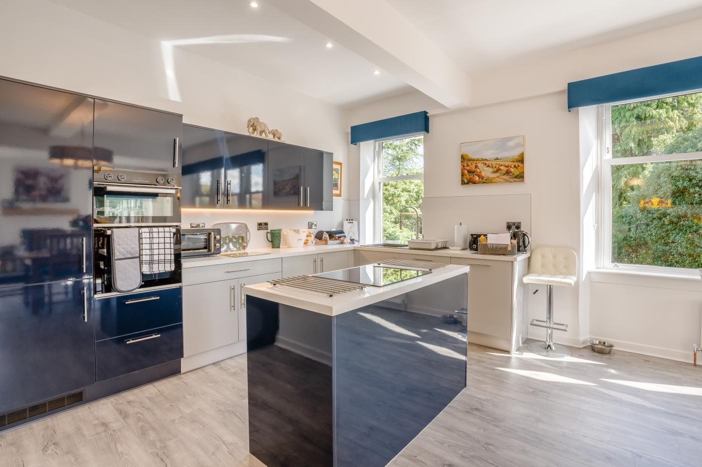 Una cocina moderna con una isla central, electrodomésticos integrados y amplias ventanas con vistas a zonas verdes.