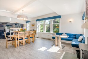Una sala de estar moderna con comedor, un sofá azul y una cocina al fondo.