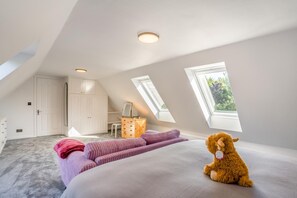 Un dormitorio en el ático con techo inclinado, tragaluces, cama, cómoda y ventana con vistas al verdor.