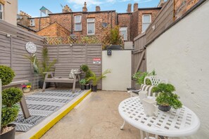 A small outdoor patio area with a wooden bench, a white table, and potted plants. - 2 Bed in Scarborough (oc-c45973) (Scarborough)
