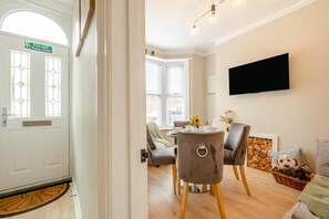 A room with a fire exit sign, a television mounted on the wall, a dining table with chairs, and a fireplace. - 2 Bed in Scarborough (oc-c45973) (Scarborough)